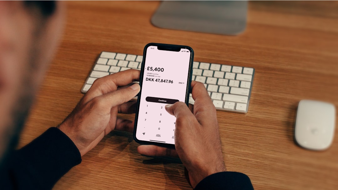 a man holding a cell phone in front of a keyboard — Photo by Atlantic Money on Unsplash