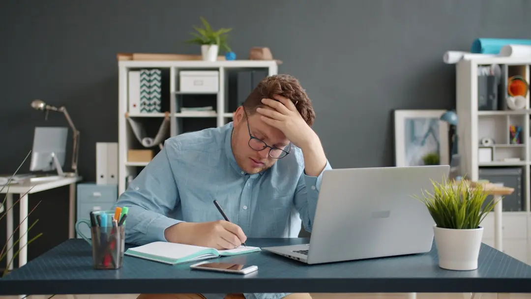 Man writing at desk with laptop, looking stressed. — Photo by Vitaly Gariev on Unsplash