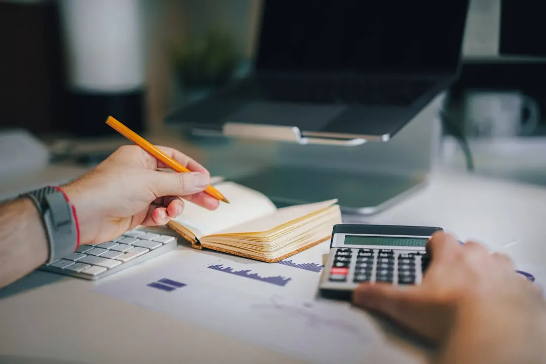 a person sitting at a desk with a calculator and a notebook — Photo by Jakub Żerdzicki on Unsplash