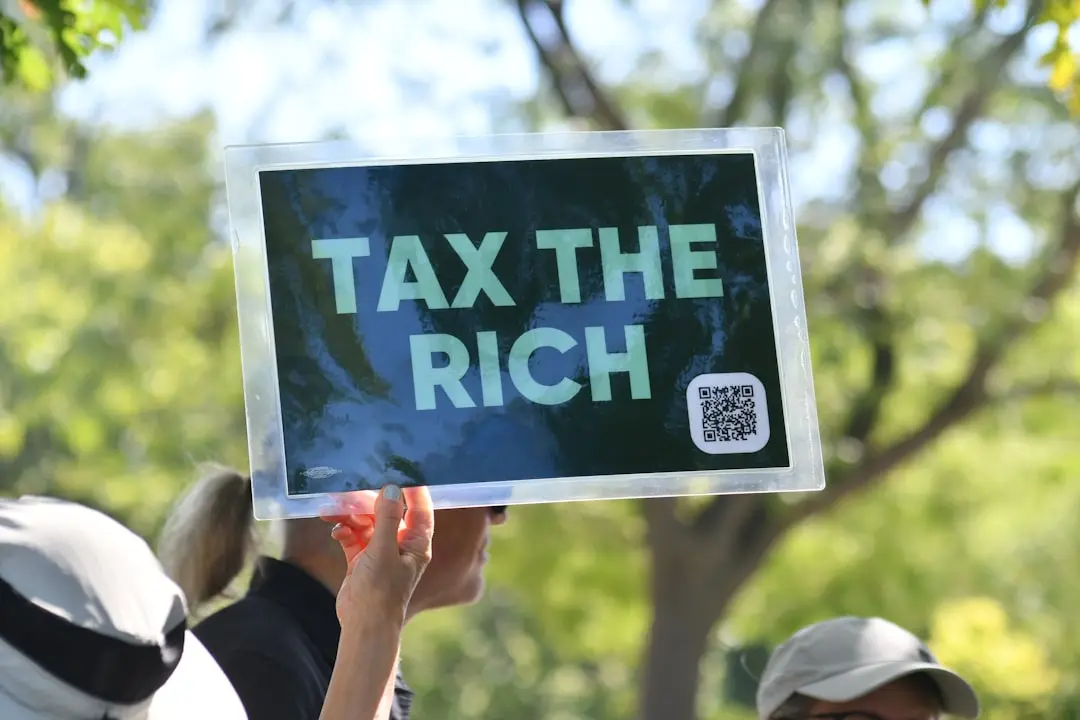 Person holds sign that says "tax the rich" — Photo by Meg on Unsplash