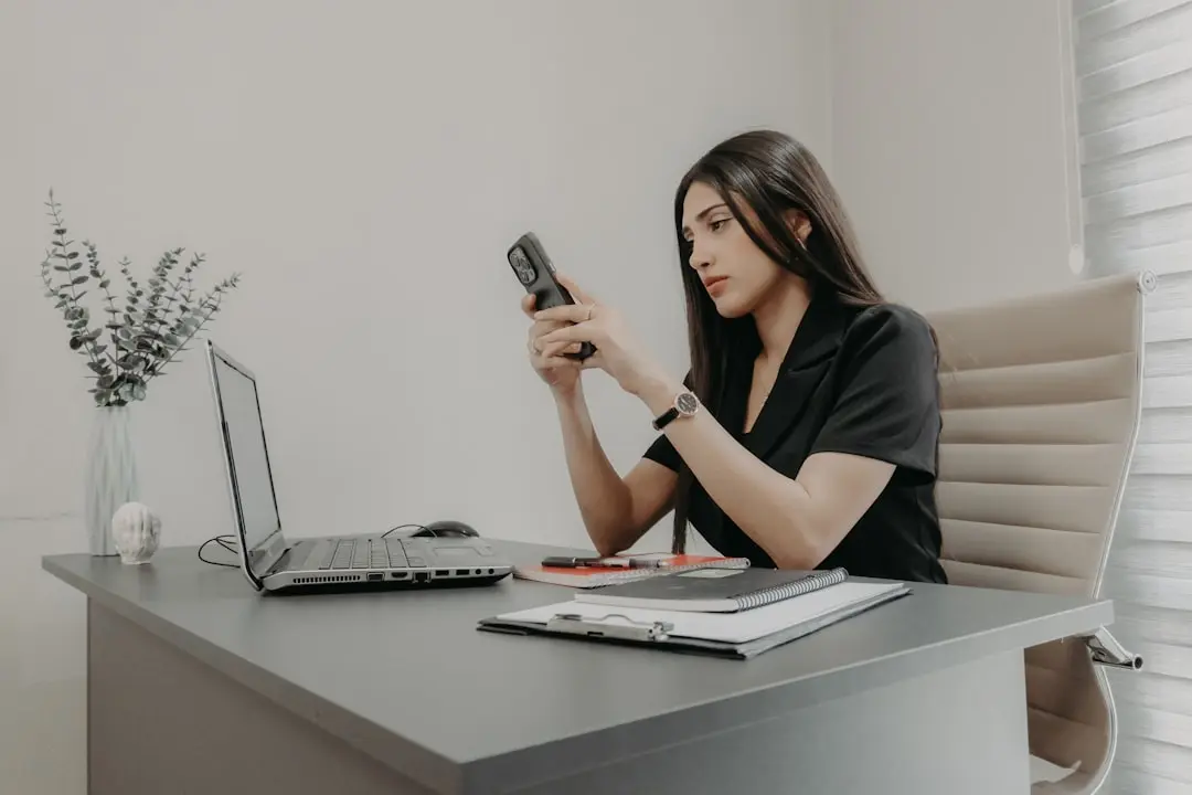 A woman using her phone at a desk — Photo by Zulfugar Karimov on Unsplash