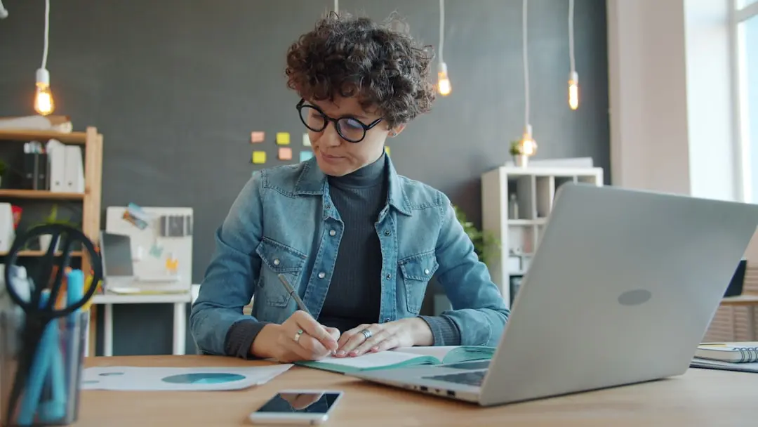 Woman with curly hair writing at desk with laptop — Photo by Vitaly Gariev on Unsplash