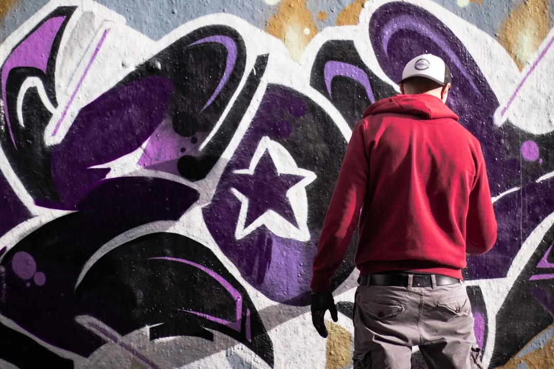 man wearing red pullover hoodie and denim jeans standing beside graffiti — Photo by François Genon on Unsplash