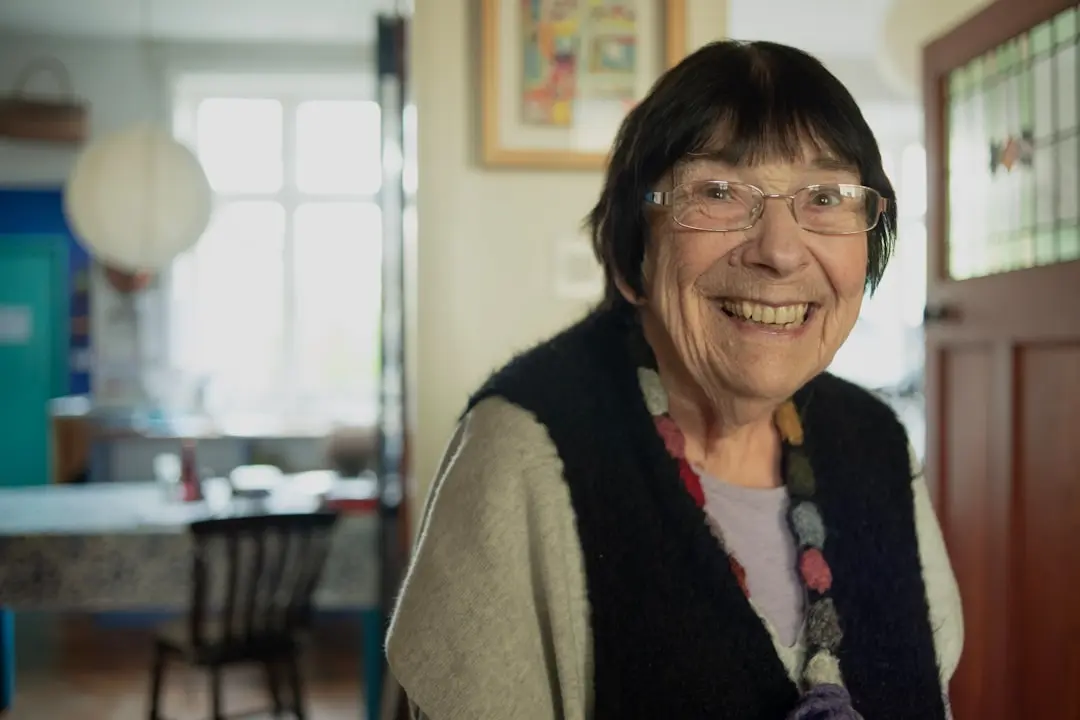 A woman with glasses smiling in a room — Photo by Age Cymru on Unsplash